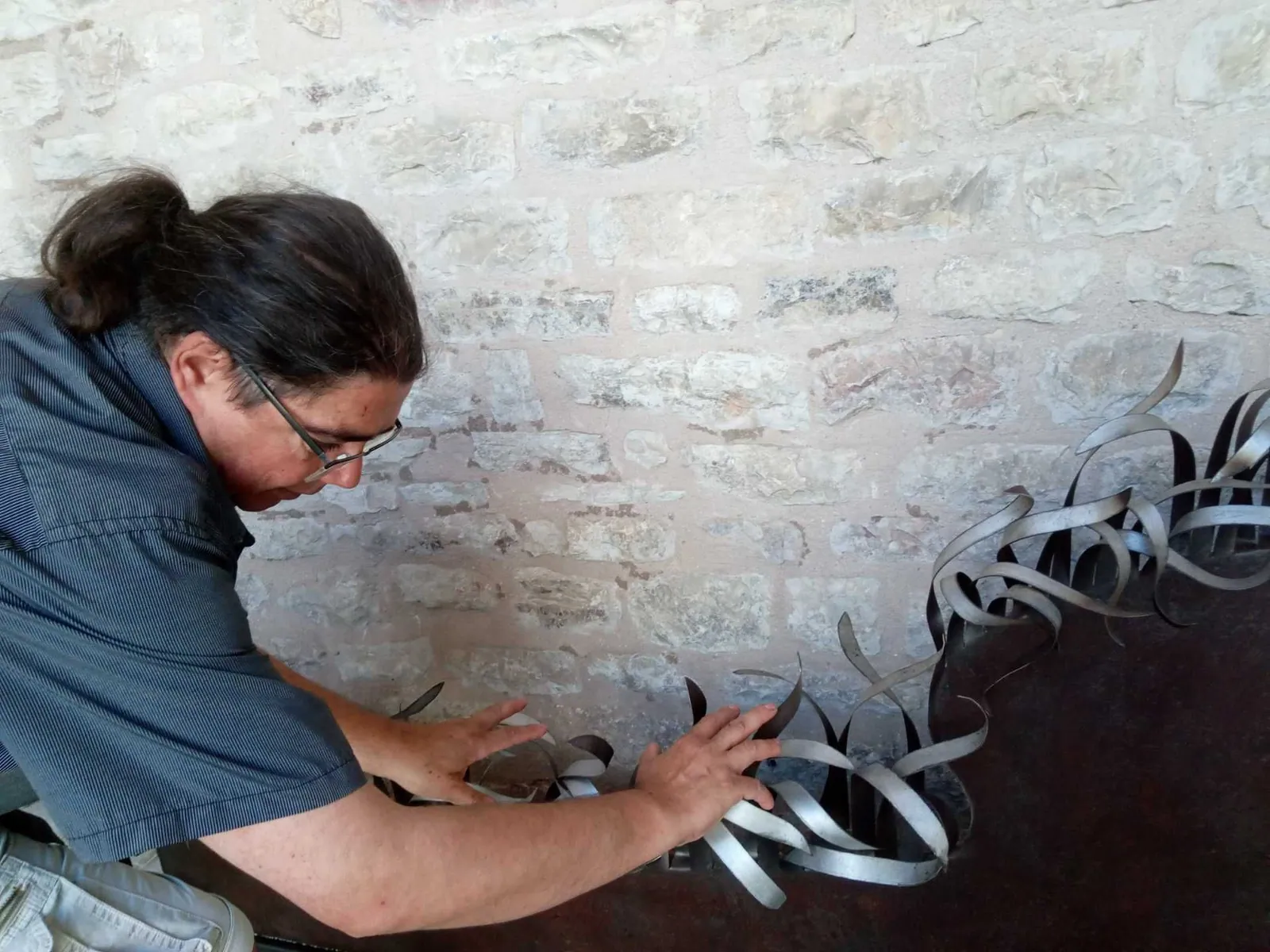 Alberto Alunni installing an iron sculpture on the stone wall of the Cloister of San Francesco in Gubbio